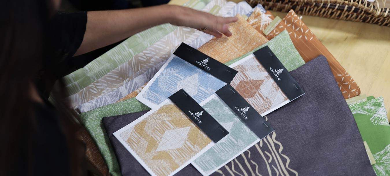 Designer Holding Hawaiian Fabric Swatches on a Table of Textiles