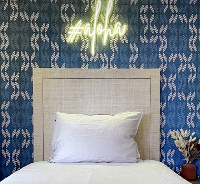 Wallcovering Product Shown With a Hawaiian Print in Blue Behind a Bed With an Aloha Neon Sign