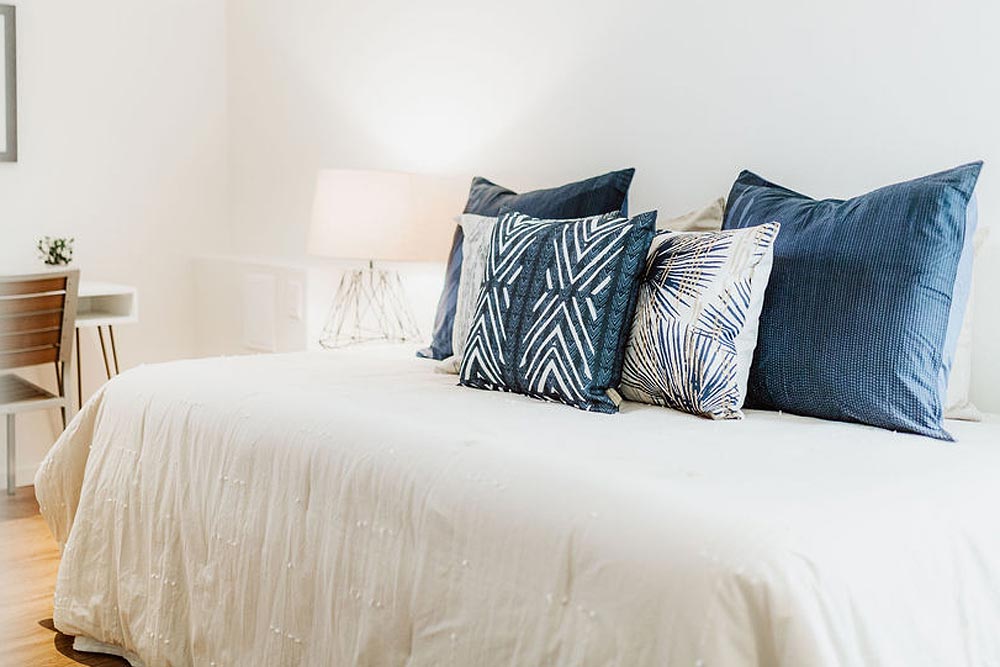 NOHO HOME Contract Residential Project Image Of Colorful Hawaiian Pillows On a White Comforter Bed